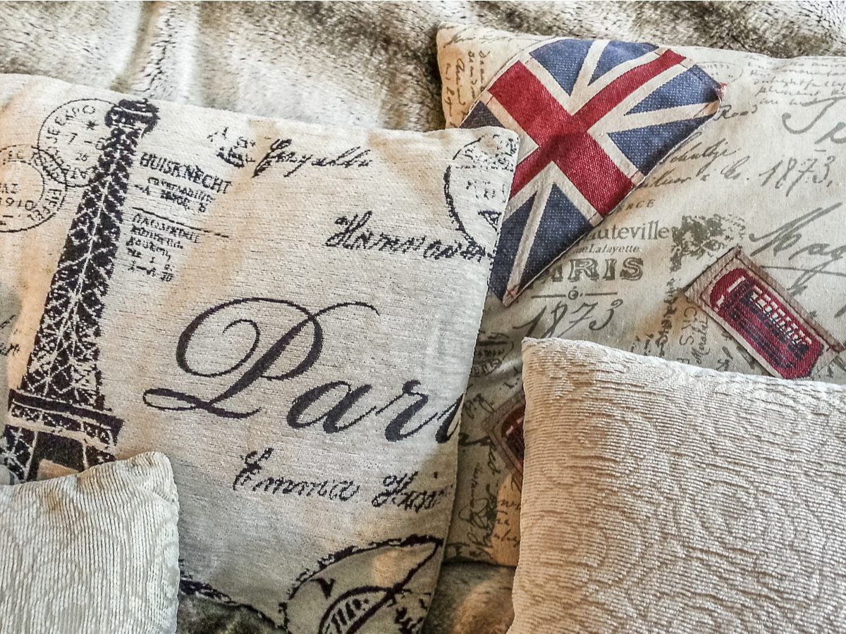 Decorative custom pillows featuring Paris motifs, such as the Eiffel Tower and elegant cursive writing, are paired beautifully with a smaller Union Jack heart pillow on a textured fabric surface.
