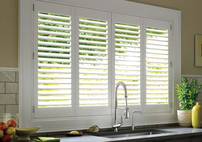Kitchen window treatments include stylish white plantation shutters that perfectly frame the scene, complemented by a sleek chrome faucet, a clean countertop, a vibrant green plant, and a cheerful yellow vase.