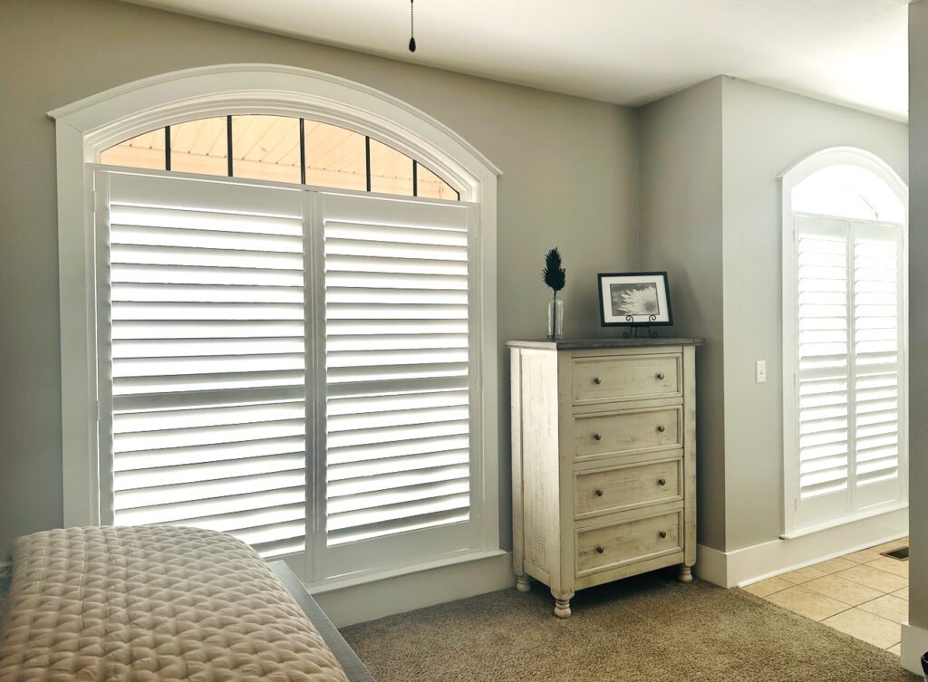 Bright Chattanooga bedroom with custom white shutters on large arched windows above a cream dresser