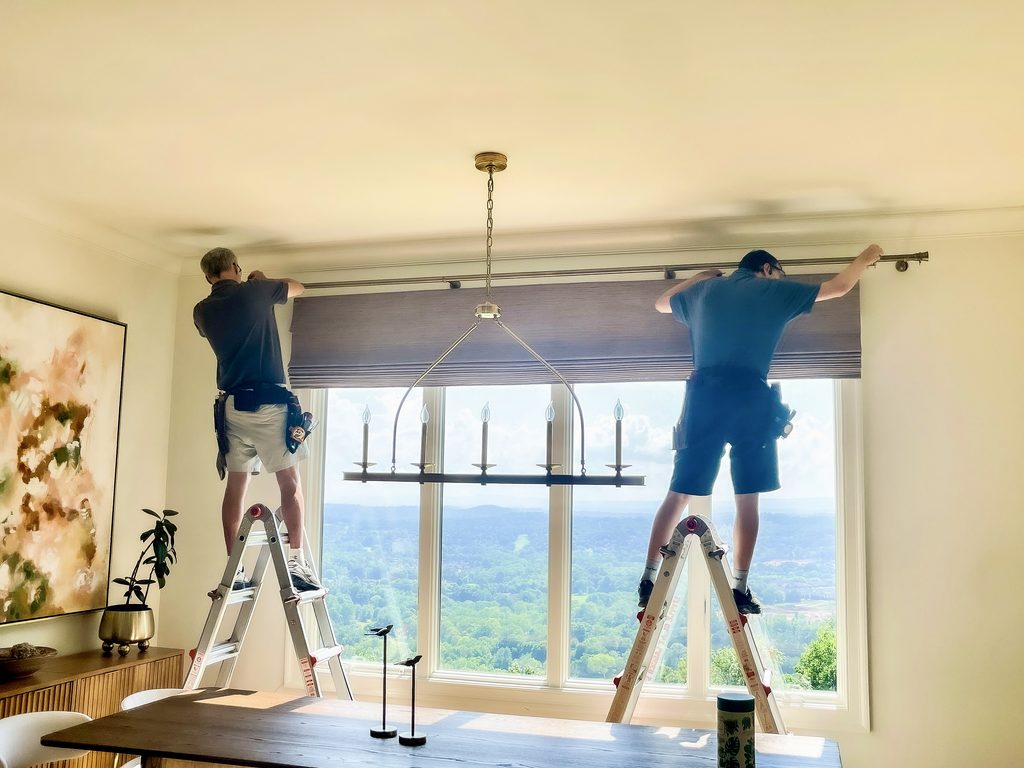 Installers hanging custom drapery on a large window during a Chattanooga window treatment install